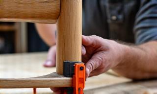 Carpenter fixing the leg of a wooden chair with clamps.